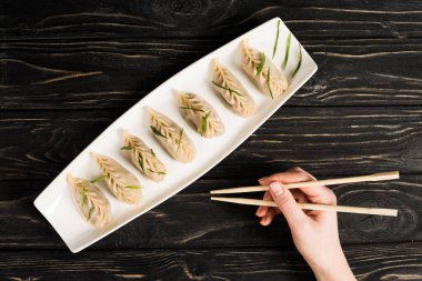 cropped view of woman eating delicious Chinese boiled dumpling with chopsticks at black wooden table clipart
