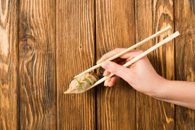 cropped view of woman holding delicious Chinese boiled dumpling with chopsticks at wooden table clipart
