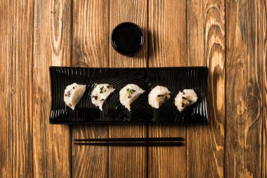 flat lay with delicious Chinese boiled dumplings on plate near chopsticks and soy sauce on wooden table