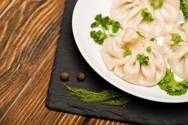 close up view of delicious Khinkali with cilantro on plate on brown wooden table