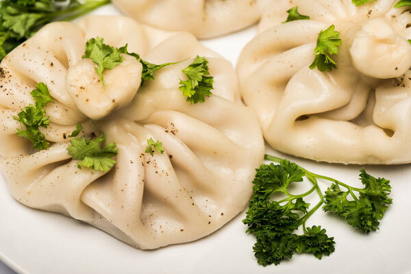 close up view of delicious Khinkali with cilantro and black pepper on white plate
