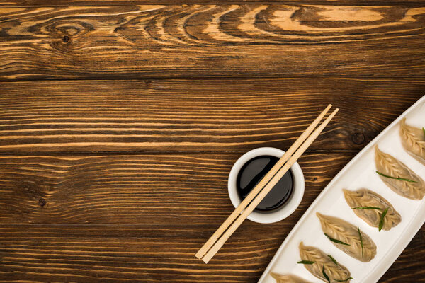 вид на вкусные китайские вареные пельмени на тарелке возле палочек и соевого соуса на деревянном столе
