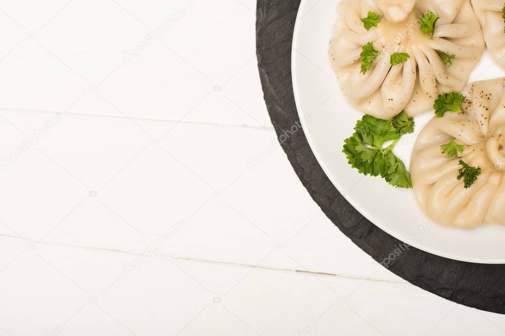 top view of delicious Khinkali with cilantro on plate on white wooden table