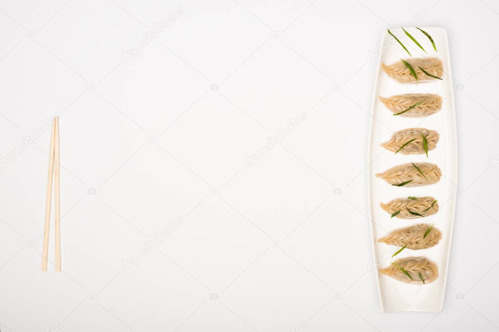 top view of delicious Chinese boiled dumplings on plate near chopsticks on white background