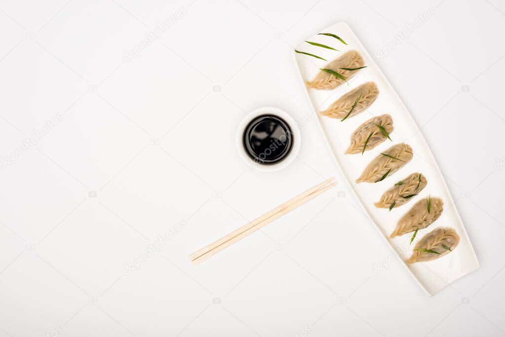 top view of delicious Chinese boiled dumplings on plate near chopsticks and soy sauce on white background