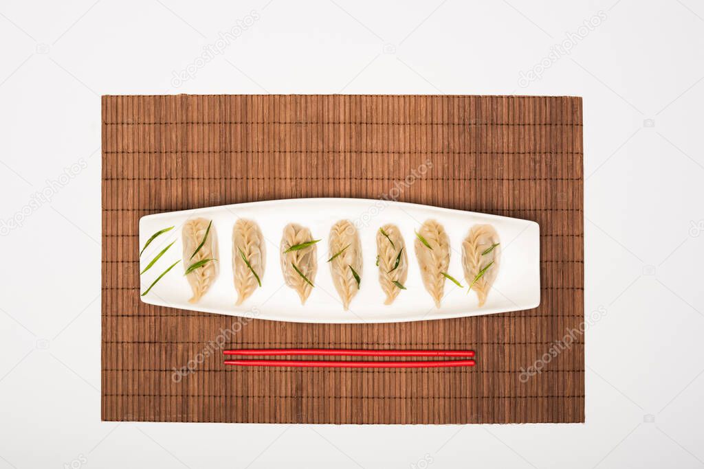 top view of delicious Chinese boiled dumplings on plate near chopsticks on bamboo mat on white background