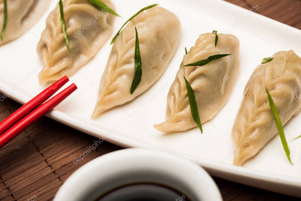 close up view of delicious Chinese boiled dumplings on plate near chopsticks and soy sauce on bamboo mat