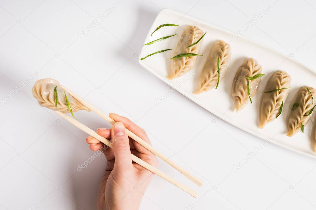 cropped view of woman eating delicious Chinese boiled dumplings with chopsticks on white background