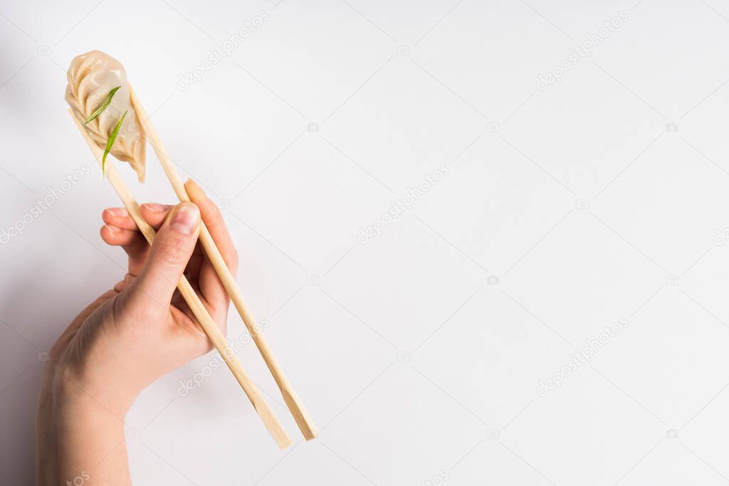 cropped view of woman holding delicious Chinese boiled dumpling with chopsticks on white background