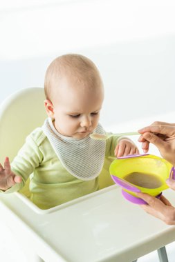 High angle view of mother with baby food feeding adorable infant on feeding chair on white background