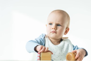 Selective focus of baby holding jars of fruit puree and looking away on white background