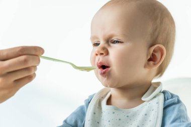 Selective focus of mother with spoon feeding baby boy on white background