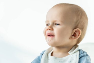 Cute baby boy with soiled mouth looking away on white background