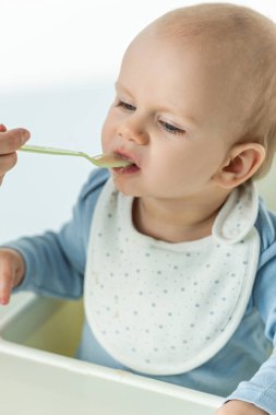 High angle view of mother feeding infant with baby food on feeding chair on white background