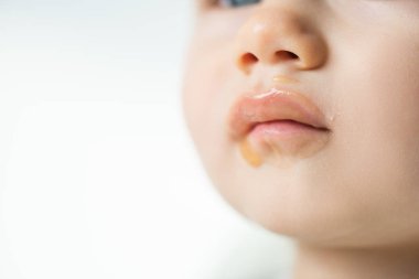 Close up view of fruit puree on soiled mouth of baby isolated on grey