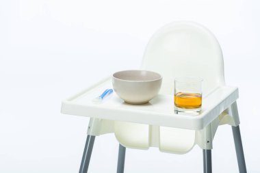 Feeding chair with bowl, spoon and glass of apple juice on table isolated on white