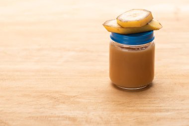 Jar of baby fruit nutrition with banana slices on wooden surface