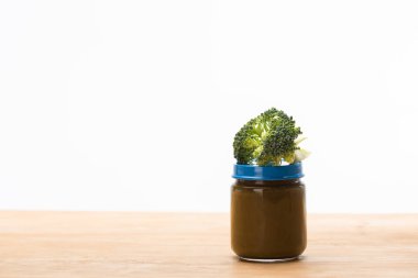 Jar of vegetable baby food with piece of broccoli on wooden surface isolated on white