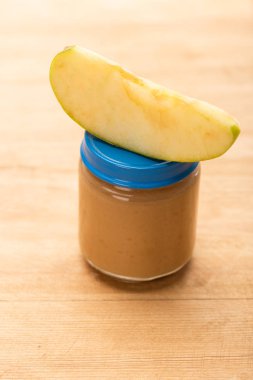 Close up view of piece of apple on jar with fruit baby nutrition on wooden surface