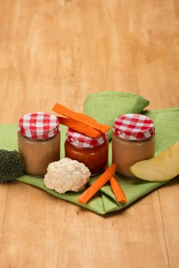 Jars of baby food with cauliflower, broccoli and carrot on napkin on wooden surface