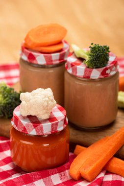 Close up view of baby food in jars with fresh vegetables on tablecloth on wooden background