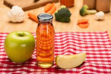 Selective focus of bottle of apple juice and baby food in jars with ingredients on tablecloth on wooden background clipart