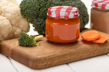 Close up view of jars with baby nutrition with vegetables on cutting board on white wooden background isolated on white