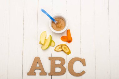 Top view of fresh ingredients near baby food and wooden letters on white wooden surface
