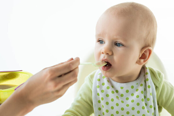 Selective focus of mother feeding adorable baby with puree isolated on white