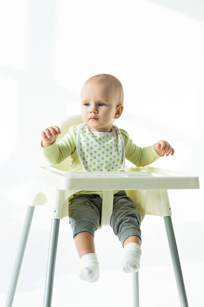 Baby sitting on feeding chair and looking away on white background