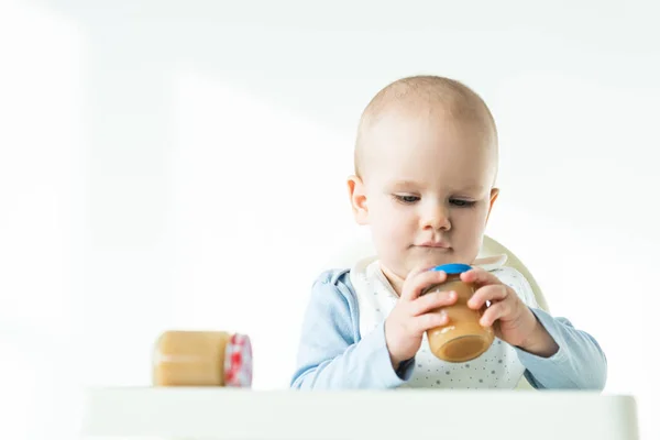 Selective focus of cute infant with jars of baby food on table of feeding chair on white background