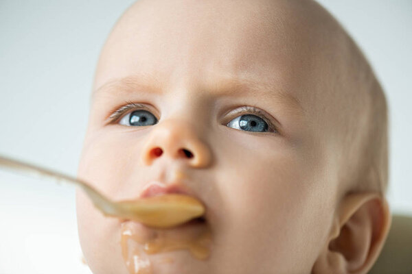 Selective focus of infant with soiled mouth during eating baby nutrition isolated on grey