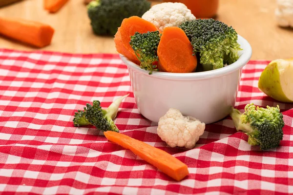 Close up view of fresh vegetables in bowl on checkered tablecloth on wooden background
