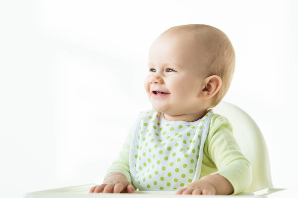 Cute baby boy smiling away while sitting on feeding chair on white background