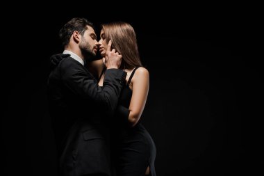 Siyah giyinmiş çekici bir kadının yüzüne dokunan yakışıklı adamın yan görüntüsü. 