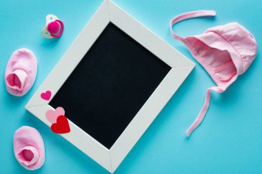 Üzerinde pembe bebek kıyafetleri ve mavi arka planda emzik olan boş karatahta manzarası, anneler günü kavramı. 