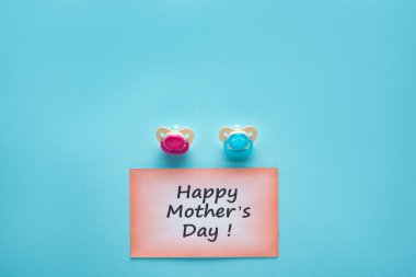 Top view of greeting card with happy mothers day lettering and pacifiers on blue background clipart