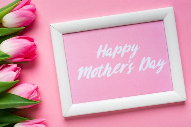 Mutlu anneler günü çerçevesinin en üst görüntüsü pembe arka planda lalelerin yanında.