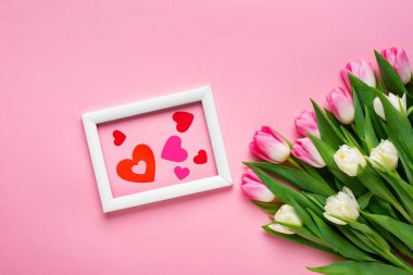 Pembe arka plandaki lale buketinin yanındaki çerçevede kağıt kalplerin üst görüntüsü