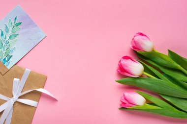 Top view of envelope, greeting card and tulips on pink background clipart