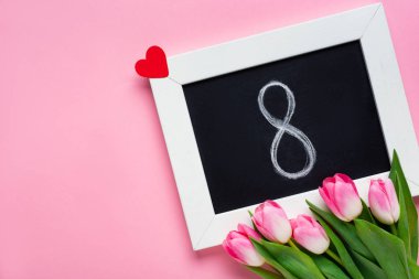 Üzerinde 8 numara olan karatahtanın üst görüntüsü, pembe yüzeyde kağıt kalp ve laleler.