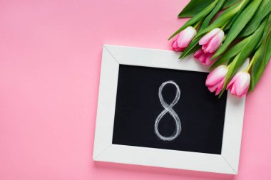 Pembe arka planda lalelerin yanında 8 rakamlı karatahtanın üst görünümü