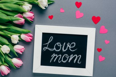 Sevgi dolu anne yazıları, kağıt kalpler ve gri arka planda laleler olan karatahta manzarası