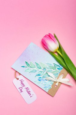 Üzerinde mutlu anneler günü yazılı tebrik kartı ve pembe arka planda lale çiziminin en üst görüntüsü.