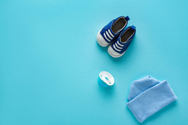 Top view of baby booties with hat and pacifier on blue background, concept of mothers day 