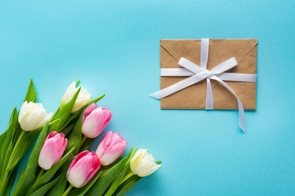 Top view of bouquet of tulips with envelope on blue background