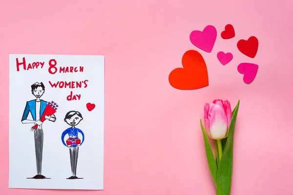 絵と8行進幸せな女性の日のレタリングとピンクの背景に紙の心を持つチューリップとグリーティングカードのトップビュー — ストック写真