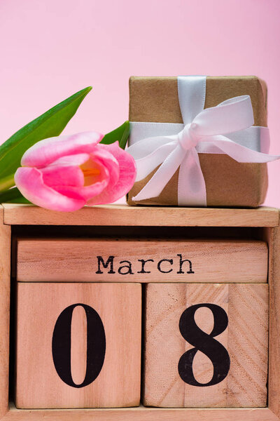 Close up view of gift box tulip on wooden calendar with 8 March date on pink background
