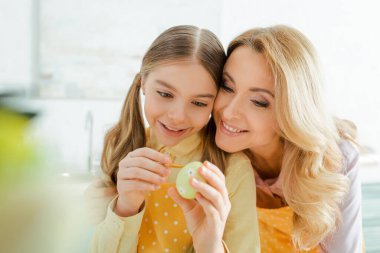 selective focus of happy mother near daughter painting easter egg 