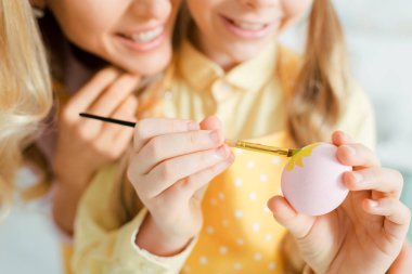 cropped view of cheerful kid painting easter egg near mother